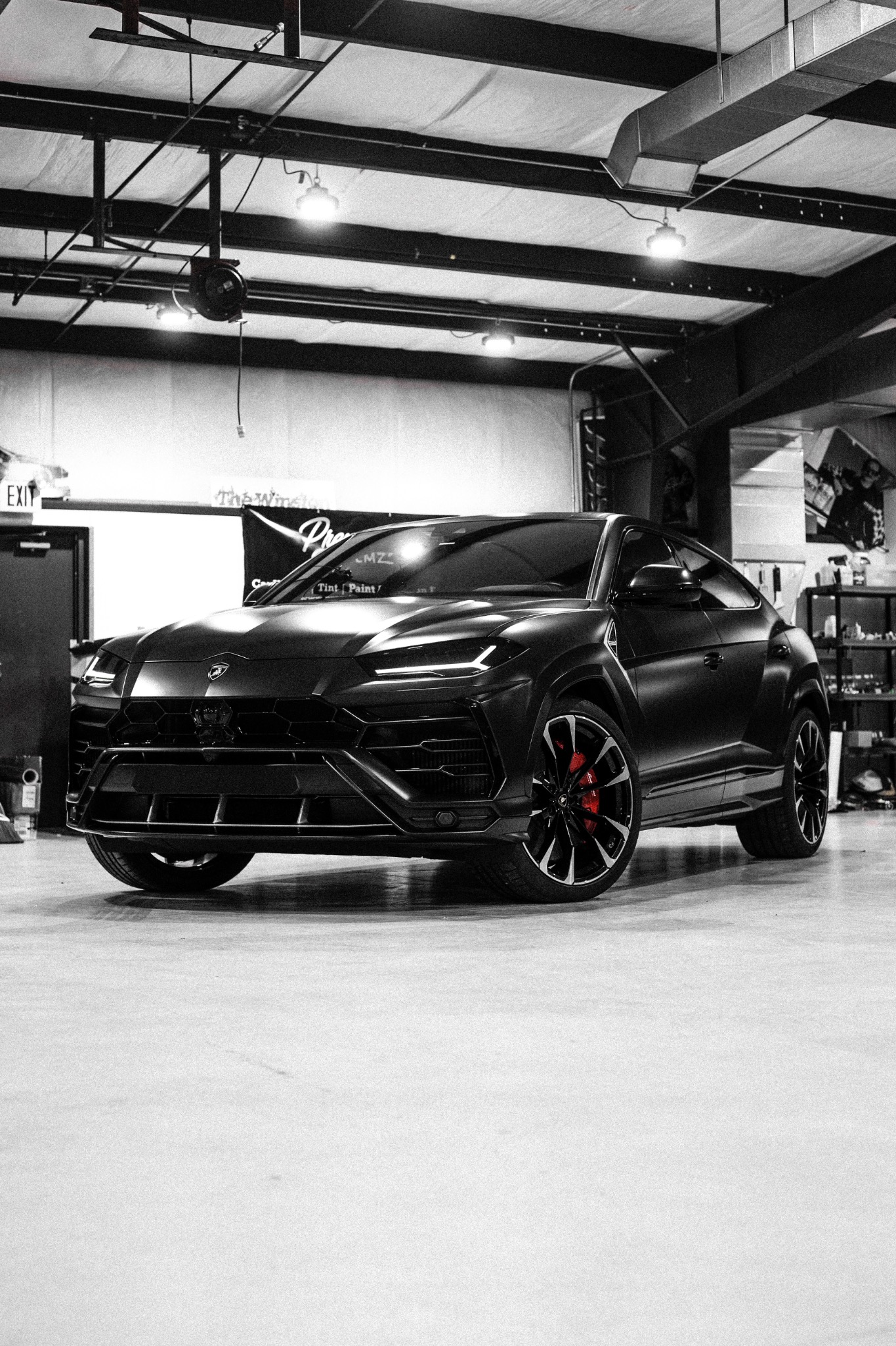 Black Lamborghini Urus beneath exposed workshop beams, with red brake calipers